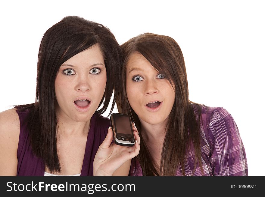 Two teenage friends are listening to a conversation on their cell phone, with shocked expressions. Two teenage friends are listening to a conversation on their cell phone, with shocked expressions.