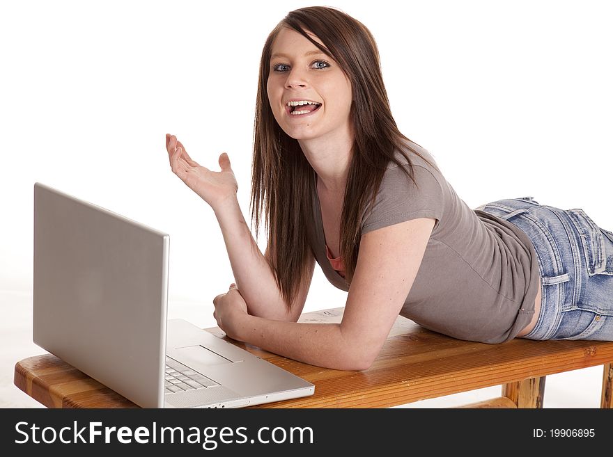 A teen laying on a bench working on her laptop. A teen laying on a bench working on her laptop.