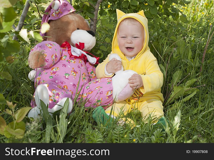 The little girl sits at a green lawn and plays with a bear cub. The little girl sits at a green lawn and plays with a bear cub