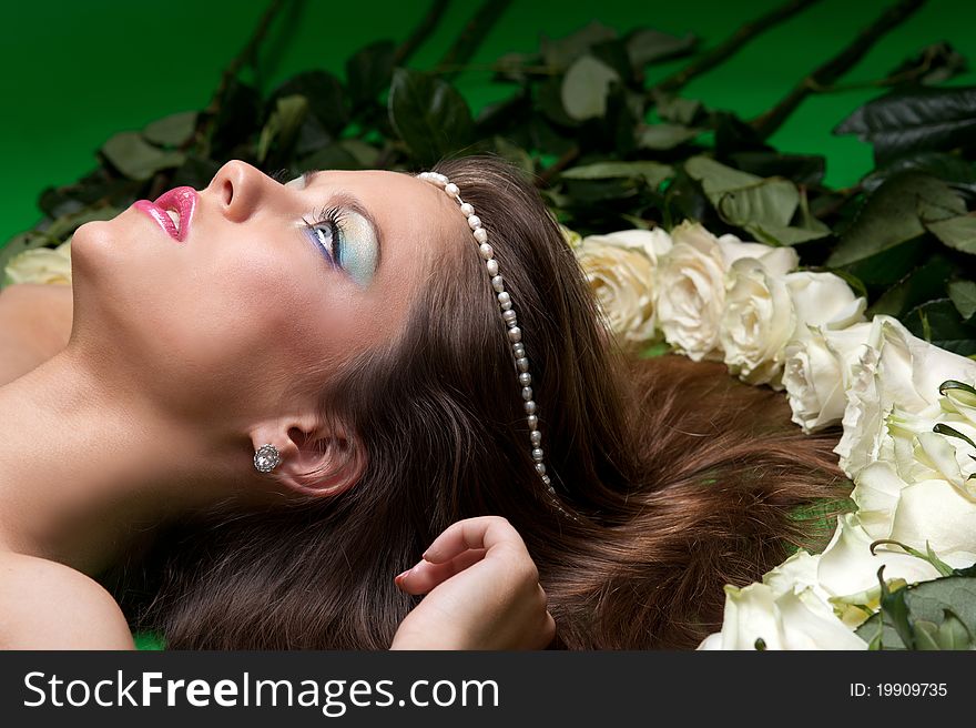 Young girl lay among the flowers of roses on a green background