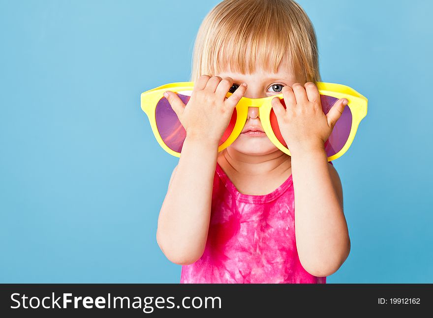 A little girl with a huge sunglasses on blue background