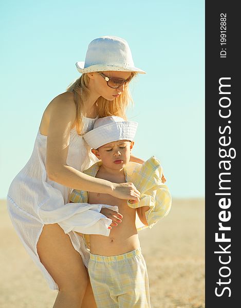 Mother dressing her son on beach while on vacation