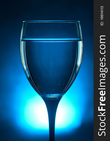 Close up shot of a glass with liquid over a blue lit background. Close up shot of a glass with liquid over a blue lit background