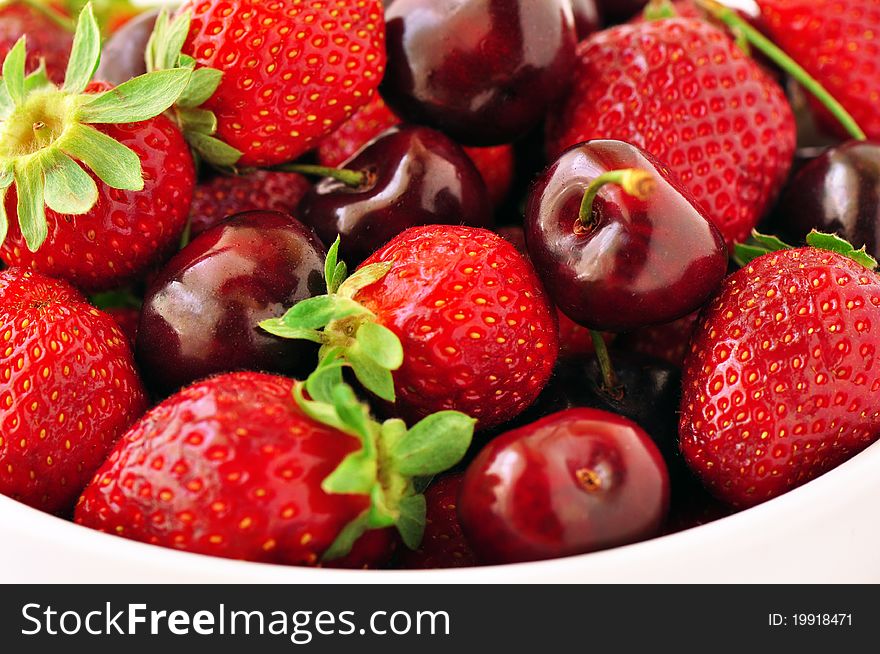 Strawberries and cherries in a bowl on a white background