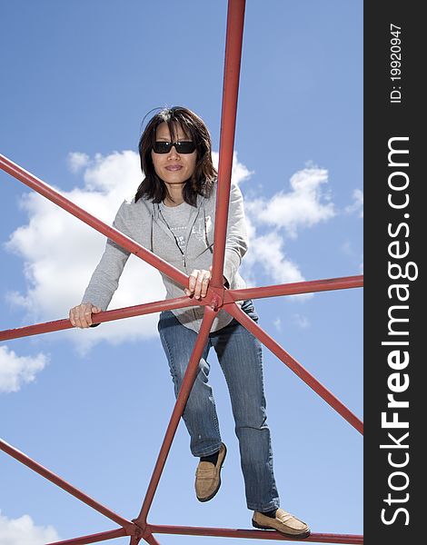 A pretty woman climbs up on a piece of playground equipment on a sunny day. A pretty woman climbs up on a piece of playground equipment on a sunny day.