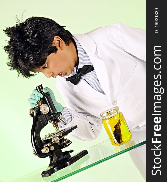 A young mad scientist shocked at what he sees through a microscope. A mouse specimen sits in a bottle nearby. A young mad scientist shocked at what he sees through a microscope. A mouse specimen sits in a bottle nearby.