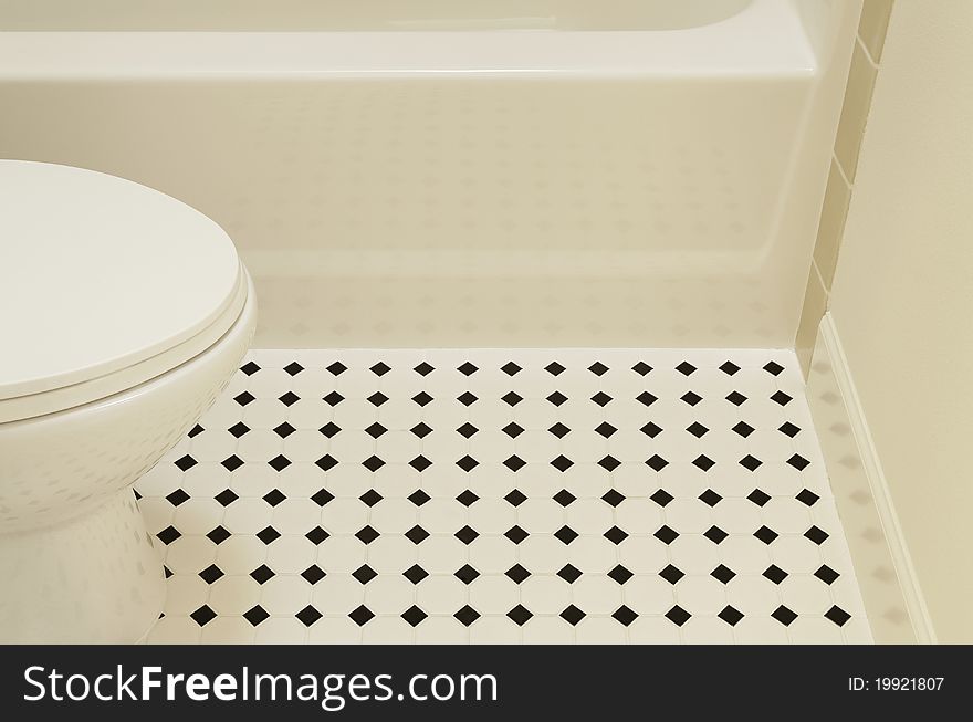 A white acrylic bathtub and porcelain toilet of a bathroom are sitting on a diamond patterned vinyl flooring in a bathroom. Horizontal shot. A white acrylic bathtub and porcelain toilet of a bathroom are sitting on a diamond patterned vinyl flooring in a bathroom. Horizontal shot.