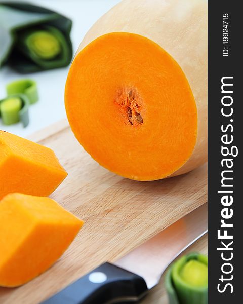 Cut pumpkin on wooden board with leek on background