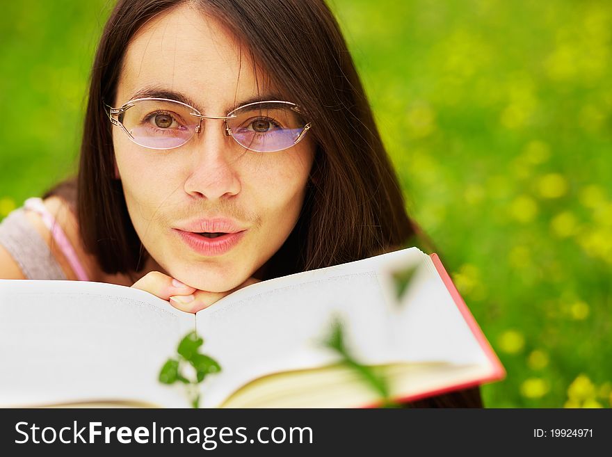 Closeup portrait of a young female with a book on a green meadow. Closeup portrait of a young female with a book on a green meadow