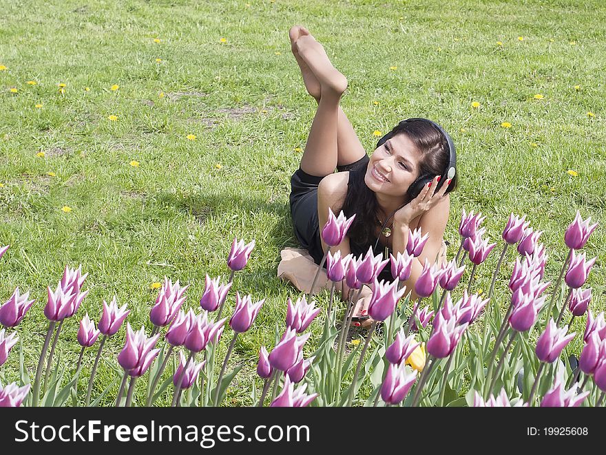 Smiling beautifull brunette on the spring grass listens to music. Smiling beautifull brunette on the spring grass listens to music