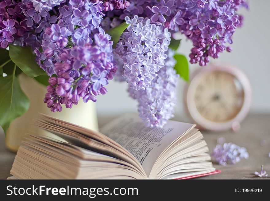 Bouquet of lilac, open book and clock