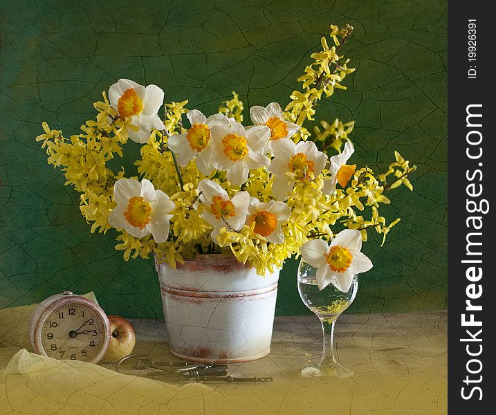 A bouquet of narcissuses is in a bucket, alongside clock and apple