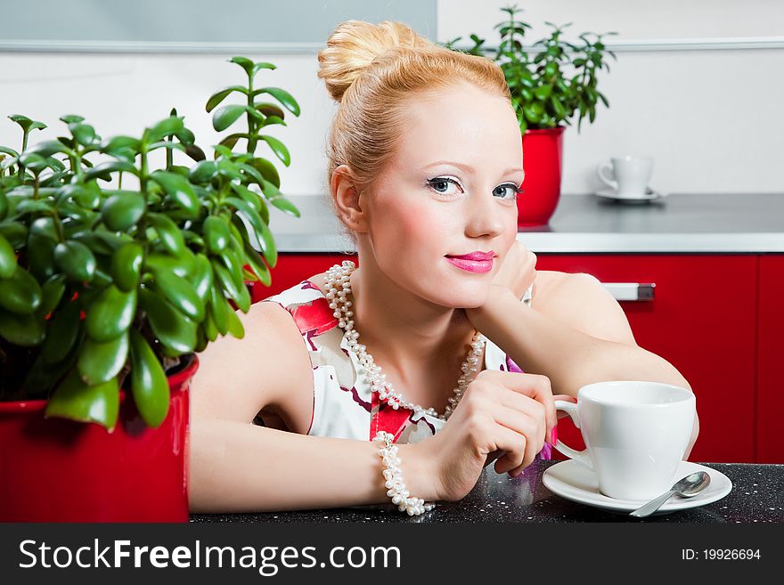 Young beautiful girl wearing white and pink dress with cup of morning coffee in interior of red modern kitchen. Young beautiful girl wearing white and pink dress with cup of morning coffee in interior of red modern kitchen