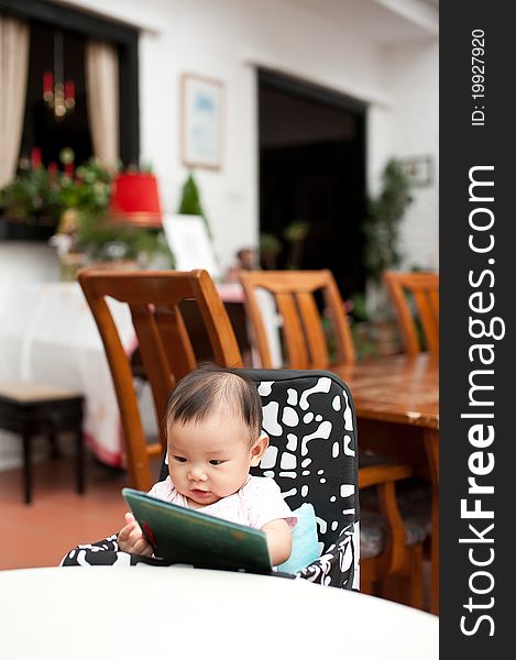 7 month old Asian baby girl reading lunch menu, sitting on a high chair