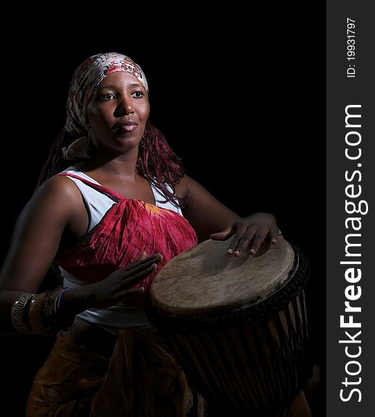 An african drummer plays a djembe drum set against a dark background. An african drummer plays a djembe drum set against a dark background