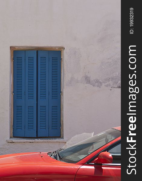 A sunlit bright red automobile constrasts with shaded deep blue shutters. A sunlit bright red automobile constrasts with shaded deep blue shutters
