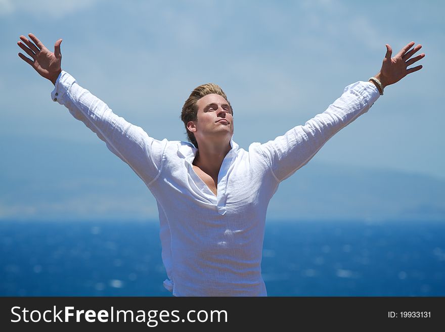 A man stands with outstretched arms on a cliffside overlooking the ocean. A man stands with outstretched arms on a cliffside overlooking the ocean.