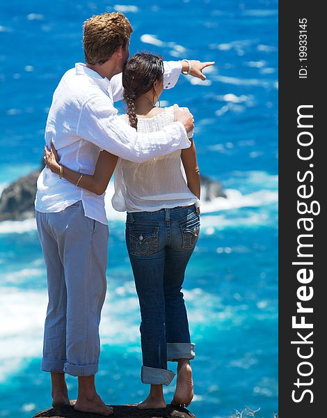 A young couple stands at the top of a cliff overlooking the ocean. The man is pointing to something in the distance. Vertical image orientation. A young couple stands at the top of a cliff overlooking the ocean. The man is pointing to something in the distance. Vertical image orientation.