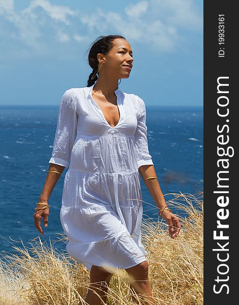 An exotic Hawaiian woman in a flowing white dress walks through tall grass on a cliffside overlooking the ocean on Maui, Hawaii. Vertical image orientation. An exotic Hawaiian woman in a flowing white dress walks through tall grass on a cliffside overlooking the ocean on Maui, Hawaii. Vertical image orientation.