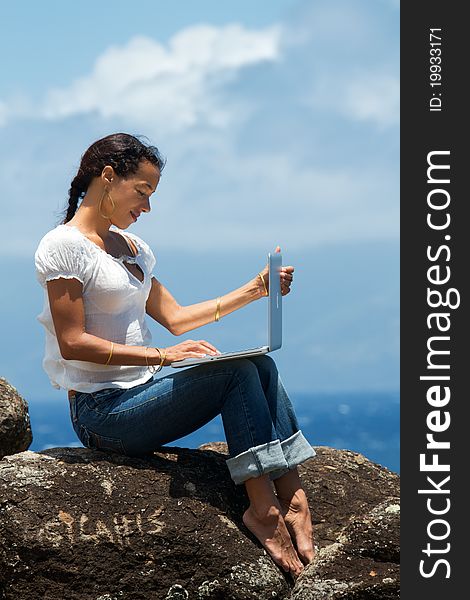 Woman works on a computer as she sits on a bluff overlooking the ocean in Maui, Hawaii. Vertical image orientation. Woman works on a computer as she sits on a bluff overlooking the ocean in Maui, Hawaii. Vertical image orientation.