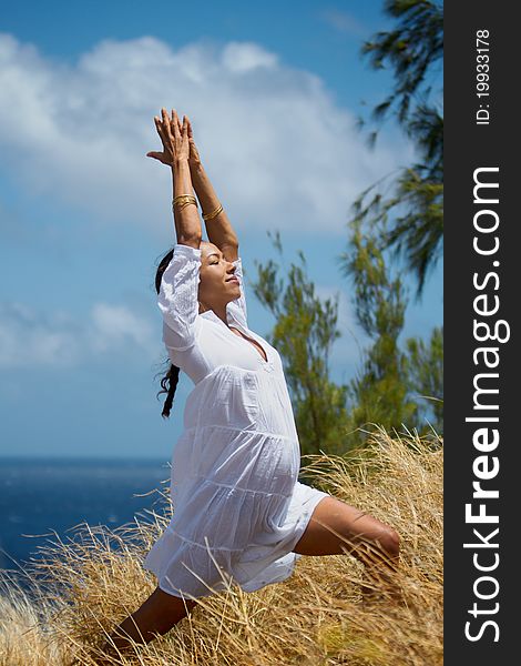 An exotic Hawaiian woman in a flowing white dress does a yoga pose in the tall grass overlooking the ocean on Maui, Hawaii. Vertical image orientation. An exotic Hawaiian woman in a flowing white dress does a yoga pose in the tall grass overlooking the ocean on Maui, Hawaii. Vertical image orientation.