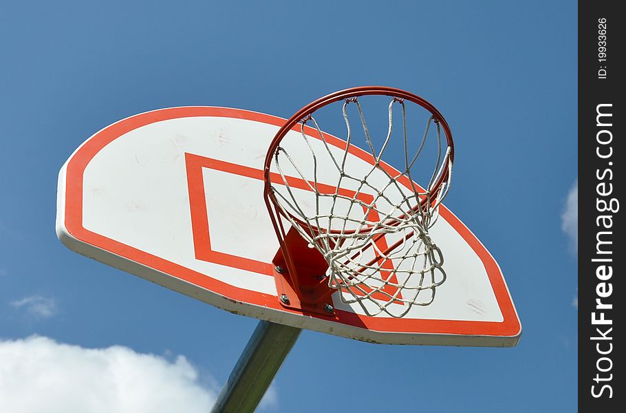 Basketball hoop with white and red backboard, against a blue sky background with a tuft of clouds