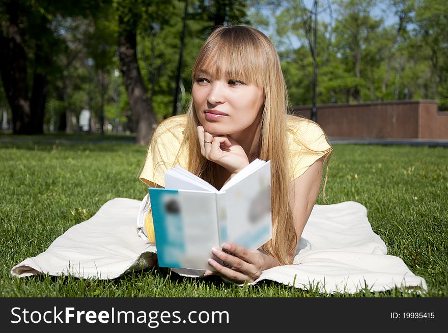 Portrait of the young girl reading in park reading on the grass. Portrait of the young girl reading in park reading on the grass