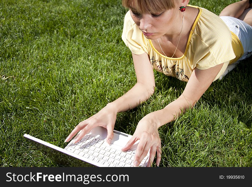 Young woman with laptop sitting on green grass in the park