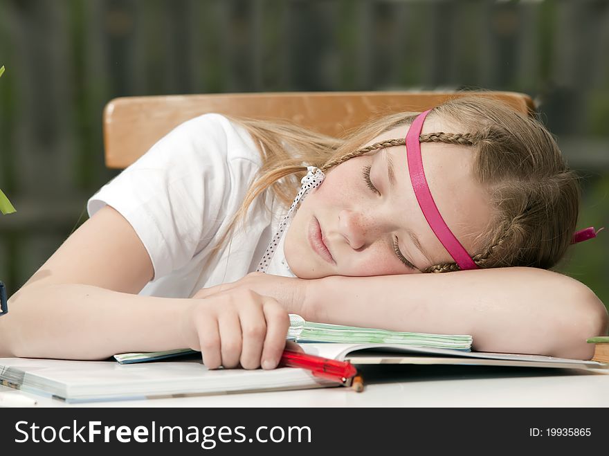 The young girl with a fair hair prepares for examinations and has fallen asleep behind books. The young girl with a fair hair prepares for examinations and has fallen asleep behind books