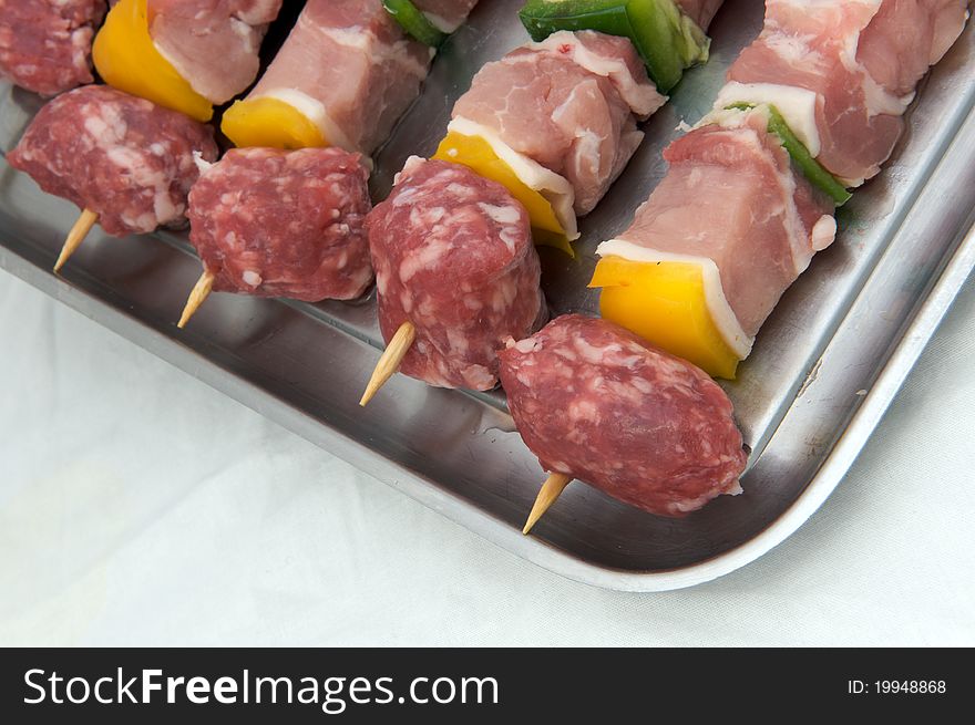 Skewers of raw meat and peppers, white background