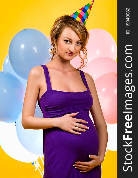 Lovely pregnant woman with party hat and balloon over yellow background