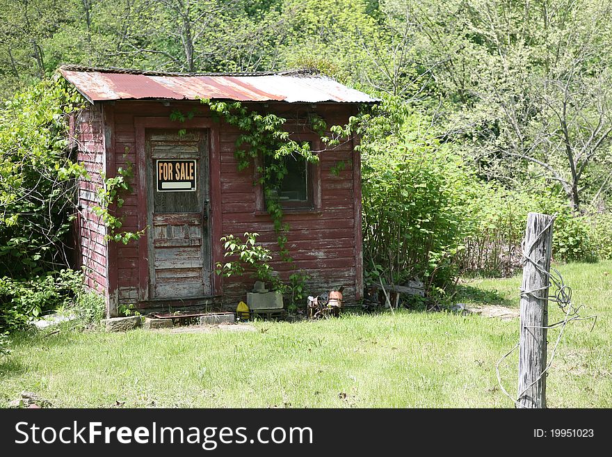 Small out building on some ones property with a for sale sign. Small out building on some ones property with a for sale sign