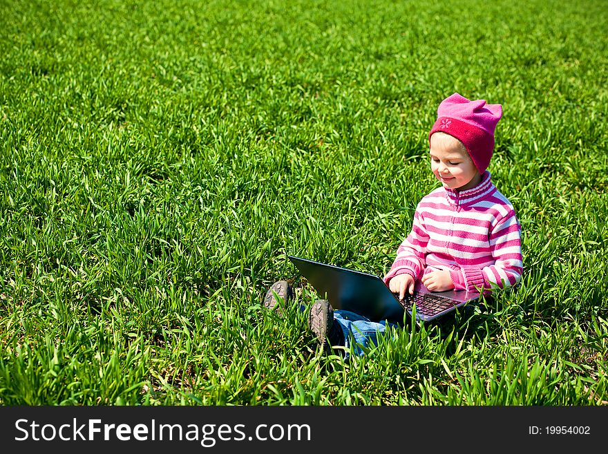 Little girl sitting with a laptop on a grass