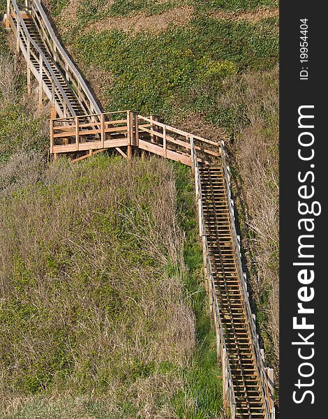 An isolated, rustic wooden staircase climbs up a steep hill. An isolated, rustic wooden staircase climbs up a steep hill.