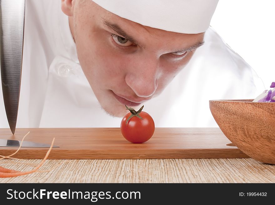 The young chef in chef's hat is considering a tomato. The young chef in chef's hat is considering a tomato.