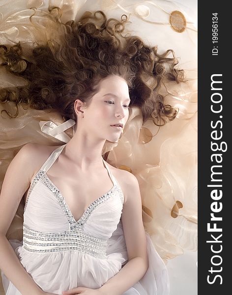 Portrait of the beautiful young woman with ringlets hairs lying on the floor in white dress