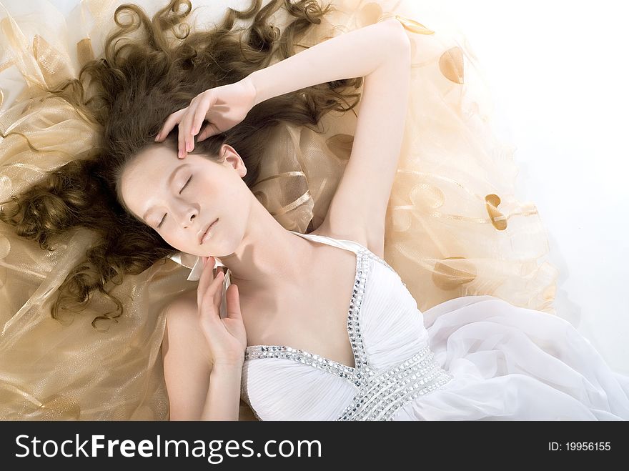 Portrait of the beautiful young woman with ringlets hairs lying on the floor in white dress