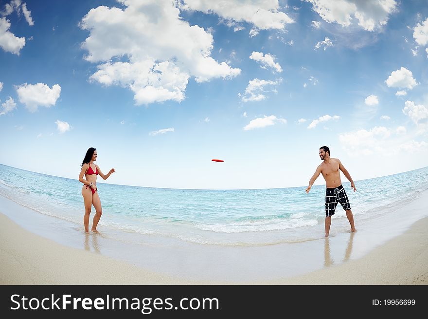 Boyfriend and girlfriend playing with frisby on tropical beach. Horizontal shape, full length, fisheye. Boyfriend and girlfriend playing with frisby on tropical beach. Horizontal shape, full length, fisheye