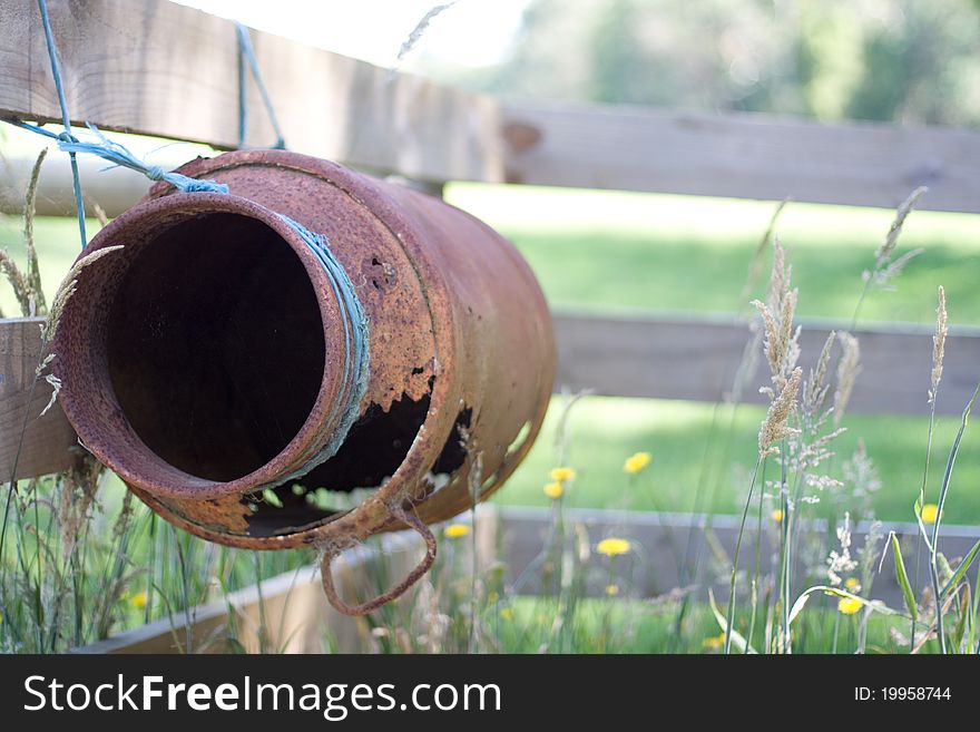 Rusty antique milk can tied to fence