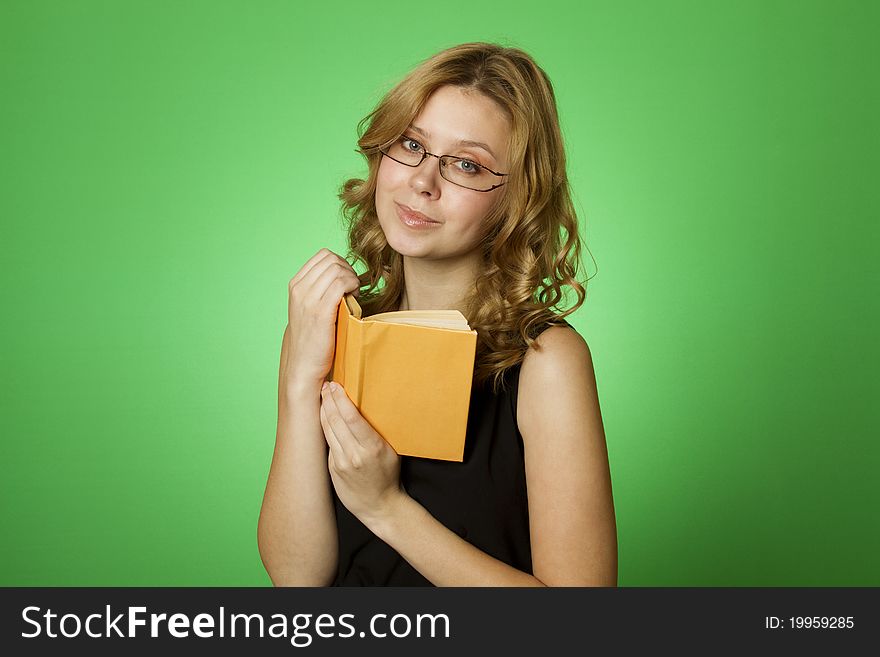 Close-up on a green background attractive girl with glasses and a little yellow book. Close-up on a green background attractive girl with glasses and a little yellow book