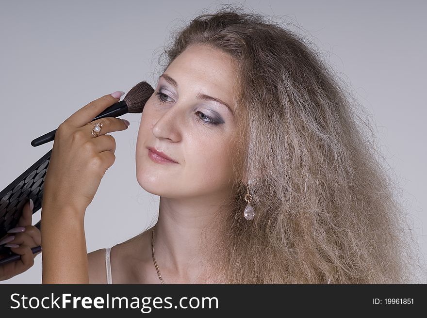 Beautiful young woman dong makeup on a gray background closeup. Beautiful young woman dong makeup on a gray background closeup