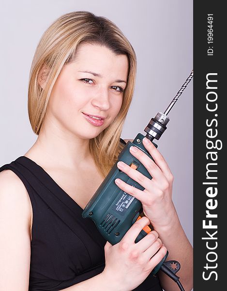 Beautiful young woman with a drill over a grey background. Beautiful young woman with a drill over a grey background