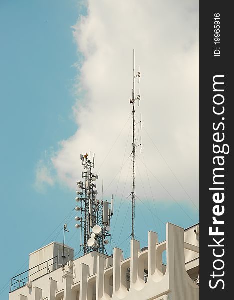 Telecommunication antenna on top of building with blue sky and clouds in the background