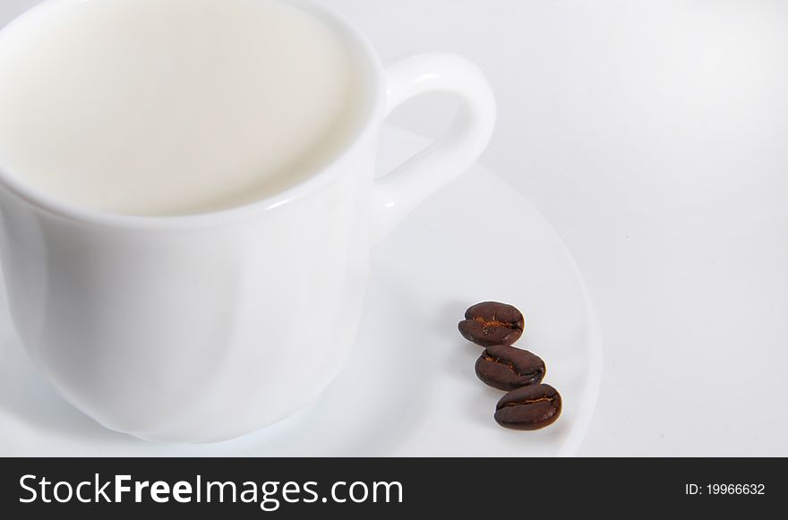 White cup with milk on white background with three coffee beans. White cup with milk on white background with three coffee beans