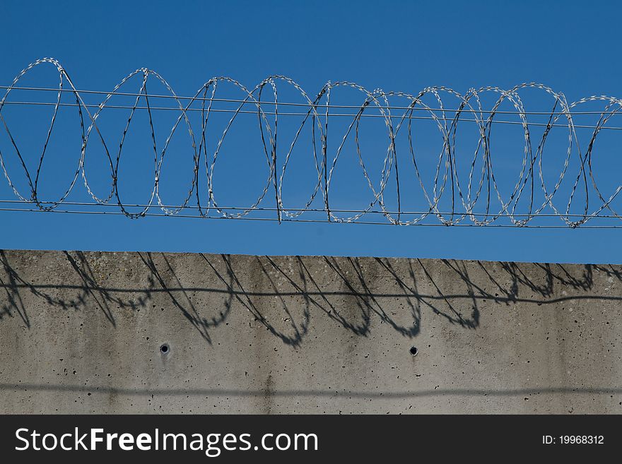 A security barrier made from spiralled razor wire and a concrete wall with a blue sky in the background. A security barrier made from spiralled razor wire and a concrete wall with a blue sky in the background.