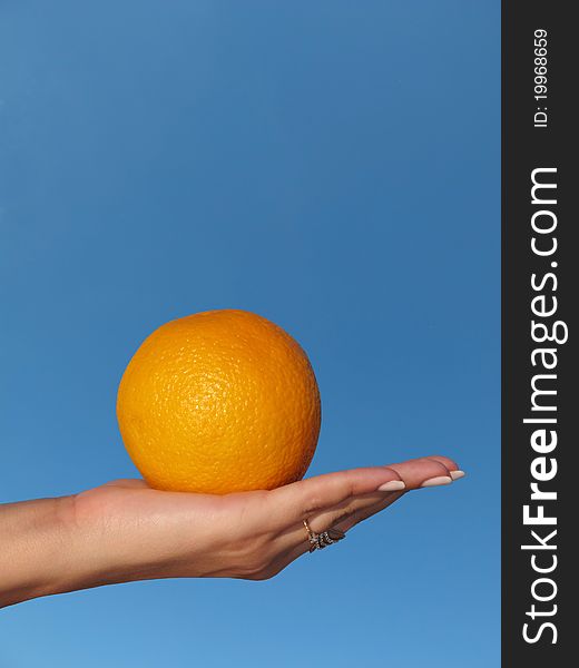 Orange in a female hand against the blue sky
