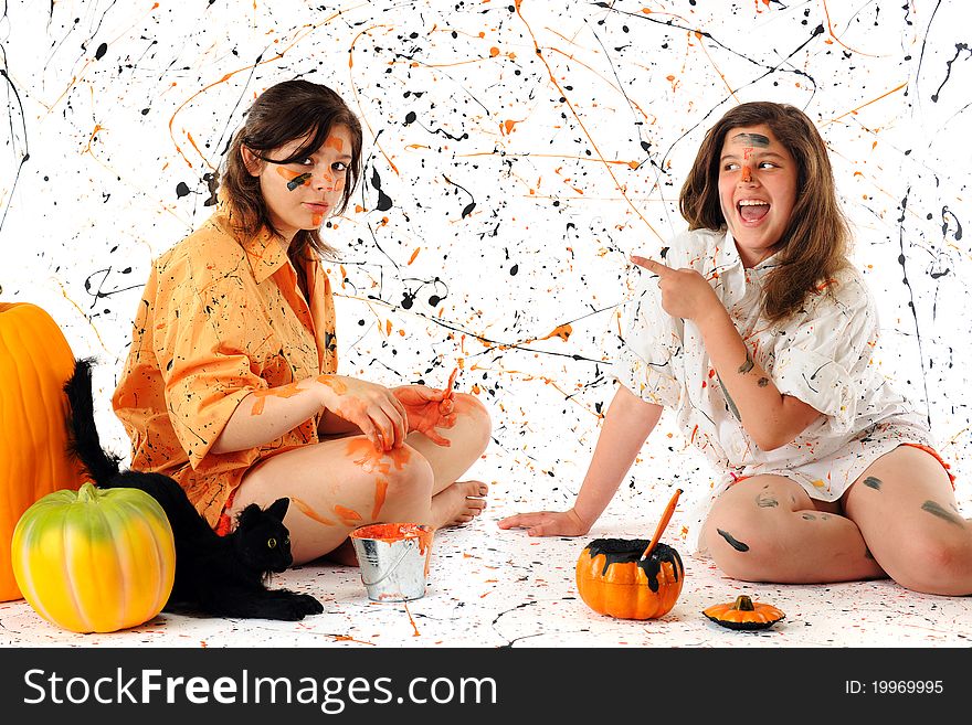 A teen and preteen making a halloween mess with black and orange pain. A black cat and pumpkins nearby. A teen and preteen making a halloween mess with black and orange pain. A black cat and pumpkins nearby.