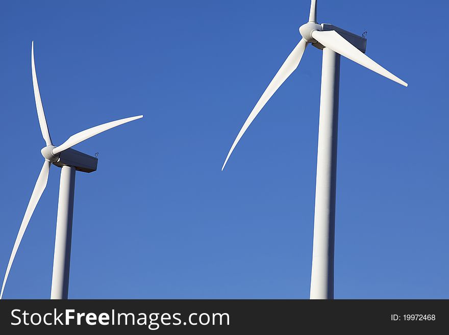 Two Wind Turbines for alternative energy production against clear blue sky. Two Wind Turbines for alternative energy production against clear blue sky