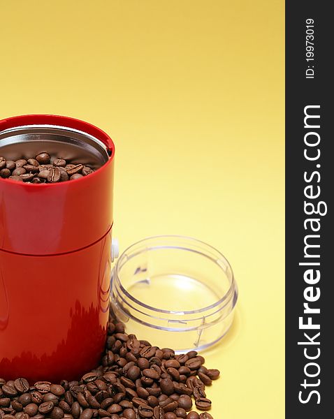 Lot of coffee beans near open modern red grinder on yellow background. Lot of coffee beans near open modern red grinder on yellow background