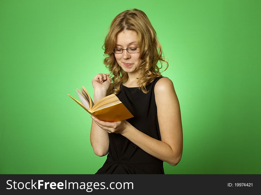 Close-up on a green background attractive girl with glasses and a little yellow book. Close-up on a green background attractive girl with glasses and a little yellow book